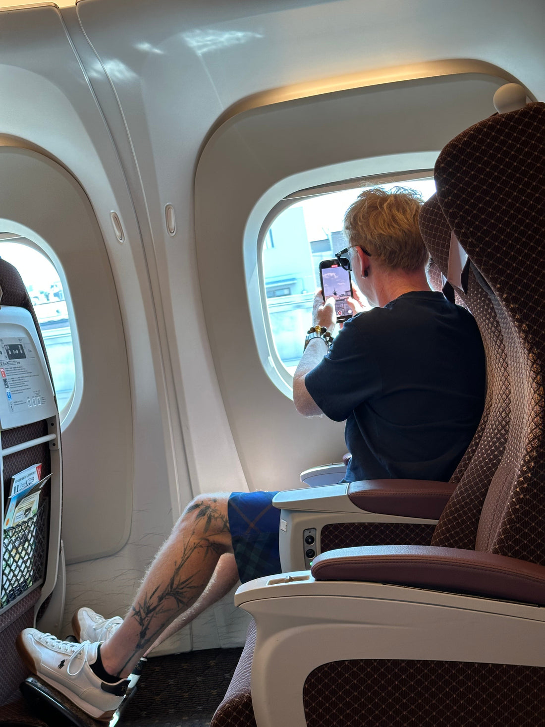 Person with leg tattoos taking a photo through train window in modern passenger seat